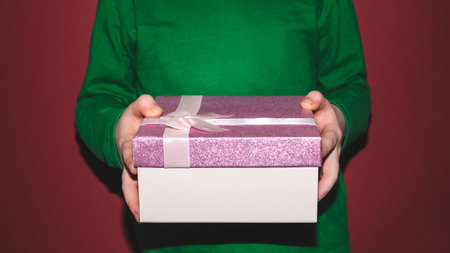 Close-up of children's hands holding a box with a gift on a red background. holiday concept.