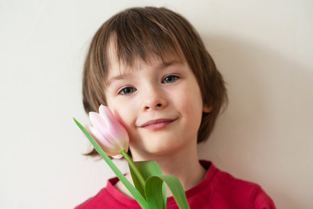 Portrait of a smiling girl with freckles in a red t-shirt with a pink tulip on a white backgroundの写真素材
