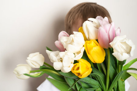 Child boy holds a bouquet of colorful tulips in front of his face on a white background.の写真素材