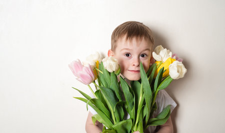 Happy smiling boy in white t-shirt with flower bouquet on white background. The concept of spring, holiday, joy, life. Copy space for textの写真素材