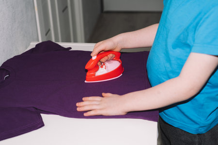 Close-up boy ironing a t-shirt with a toy iron. housework, helper. child development conceptの写真素材