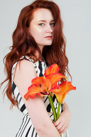 young beautiful woman has red hair creative gold make up are posing in a studio with flowers