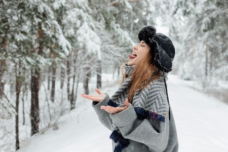 Beautiful young woman standing among snowy trees in winter forest and enjoying snow.の写真素材