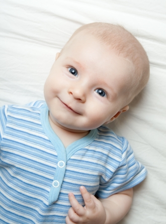 Happy little boy lies on the bed sheetの写真素材