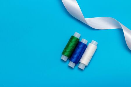 white, blue, green thread and ribbon on a blue background, copy space, top view