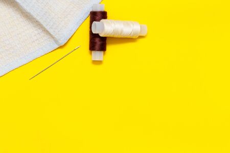 fabric, brown and beige thread, needle, on a yellow Sunny background, top view, place for text,...