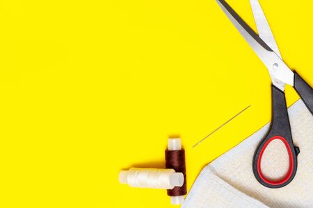 fabric, brown and beige thread, needle, scissors on a yellow Sunny background, top view, place for text, copyspaceの写真素材