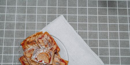 puff pastry puffs with Apple, cinnamon and powdered sugar, in a plate on the table with a checkered tableclothの写真素材