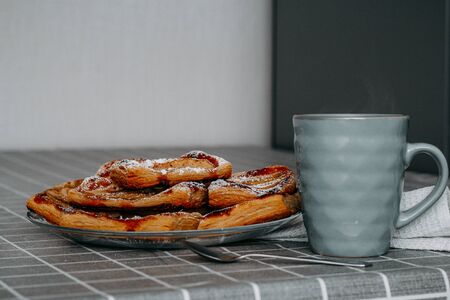 puffs of puff pastry with Apple, cinnamon and powdered sugar, in a plate on the table with a checkered tablecloth, red tea in a turquoise mug, a spoonの写真素材