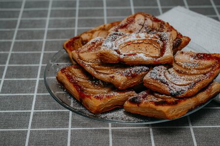 puff pastry puffs with Apple, cinnamon and powdered sugar, in a plate on the table with a checkered tableclothの写真素材