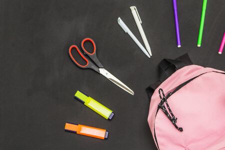 preparing for school, on a black background are colored markers, scissors, markers, pens and a pink...