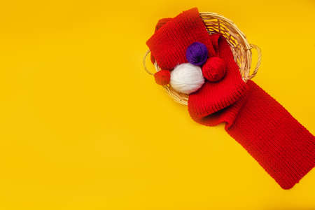 on an orange background, a wicker basket, through which a red knitted scarf is stretched, in the basket skeins of woolen threads of blue and white colorsの写真素材