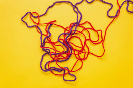 on a yellow background are red and blue wool knitting threads that are intertwined
