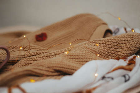 a beige woolen knit sweater and a light brown cotton scarf lie on the table. On top is an led garland. side viewの写真素材