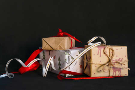 on a black background are Christmas gifts wrapped in wrapping paper and tied with ribbons, a small...