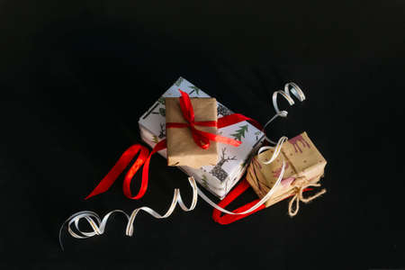 on a black background are Christmas gifts wrapped in wrapping paper and tied with ribbons, a small...