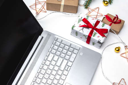 Christmas online shopping. An open laptop on a white background, gift boxes tied with a red ribbon, green fir branches, garlands of stars. Online trading during the winter holidays.の写真素材