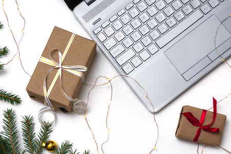 Christmas online shopping. An open laptop on a white background, a credit card, gift boxes tied with a red ribbon, green fir branches, garlands of stars. Online trading during the winter holidays.の写真素材