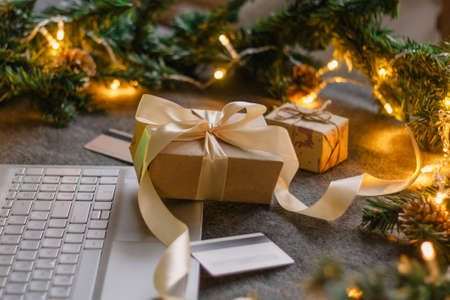 Christmas shopping online with a credit card for the holiday. Laptop with gifts on the table next to...