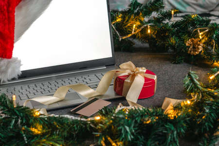 Christmas shopping online with a credit card for the holiday. Laptop with gifts on the table next to fir branches and a garland of lights.の写真素材