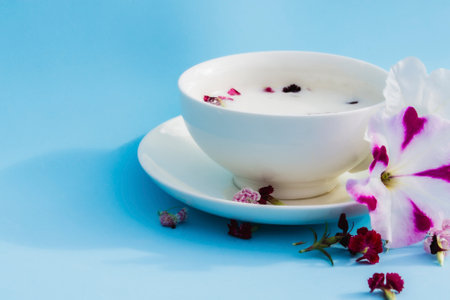 White Cup with vegan milk and flowers on a blue background. Concept of vegetarian drinks and food, herbal teas, beauty and health, Spa.の写真素材