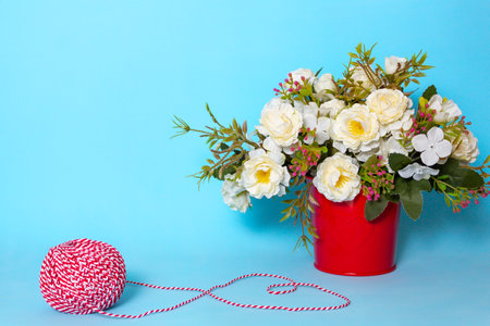 flowers for interior decoration in a red pot on a blue background, next to a white-red thread.