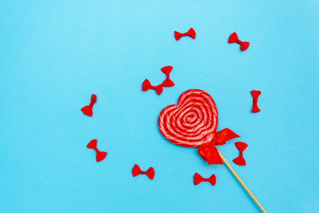 Lollipop with a bow on a blue background. bows in the shape of a heart. Copy space. Top view flat lying.の写真素材