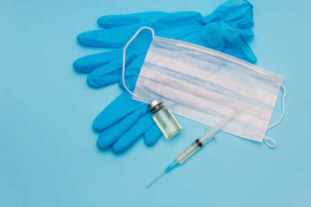 The vaccine is in a jar next to a syringe, a medical mask and blue gloves on a blue background.の写真素材