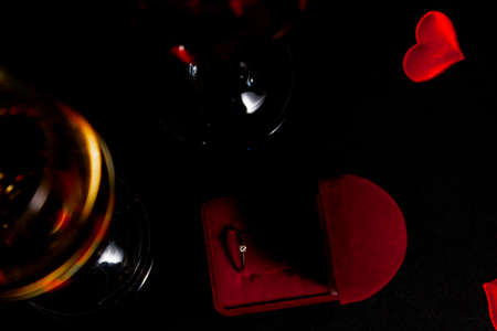 two glasses of champagne stand in the dark, next to a box with a ring to make a marriage proposal, and confetti from hearts. selective focus, top view.の写真素材