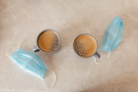 a couple of cups of coffee on the table, next to the medical masks. The concept of lifestyle, a new...