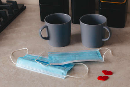 A pair of coffee cups sitting on the table, cogni next two medicinskie masks and confetti of hearts red. A way of life, a new reality. The concept of home comfort and meetings.の写真素材