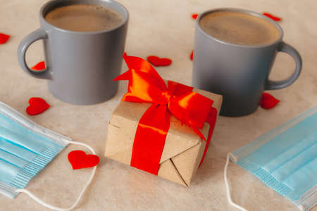 two gray coffee cups sit on the table, next to a gift box with a red bow, medical masks, and...