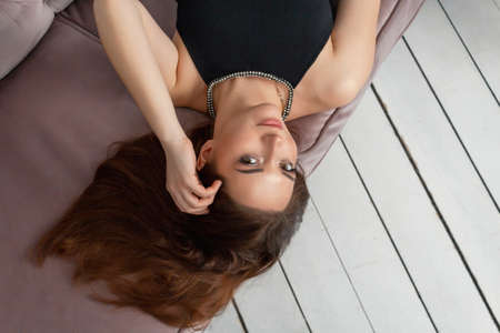 A happy, beautiful, successful woman with long hair lay down on a sofa in a black dress. Portrait,...