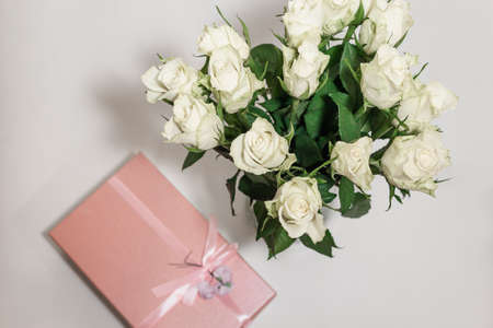 White tea roses stand in a glass vase, which is tied with a red ribbon and stands on the table....