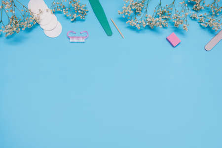 Manicure tools on a blue background are decorated with white gypsophila flowers. The concept of...