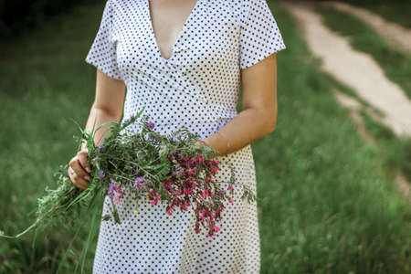a girl in a white light dress holds a bouquet of wild flowers in her hands. depersonalized photo,...