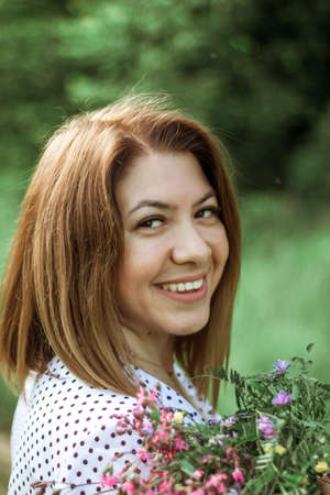 A girl with a short haircut laughs and holds flowers in her hands. A close portrait from the back of...