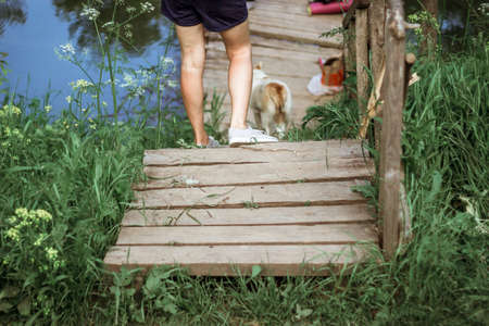 the legs of a girl with a dog go down the stairs to the bridge on the river.の写真素材
