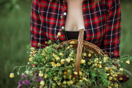 Summer lifestyle portrait of a beautiful young woman smiling and holding a basket with a bouquet of wild flowers. The concept of happiness and love. Photo without a head.の写真素材