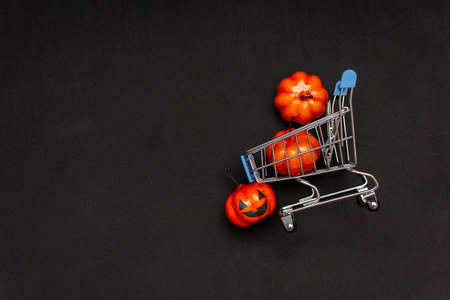 A cart with orange pumpkins on a black background. flat lei on the topic of sale in halloween. copy space.の写真素材