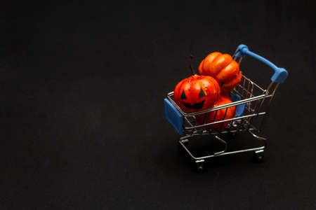 A cart with orange pumpkins on a black background. flat lei on the topic of sale in halloween. copy space.の写真素材