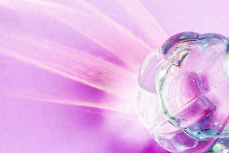A glass vase on a light lilac background with hard shadows and sun glare. Reflection of light from glass. Abstract background.の写真素材