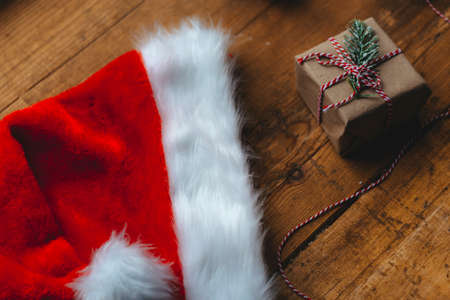Stylish packaged Christmas gift box, Santa Claus hat and a sprig of spruce on a rustic wooden table....