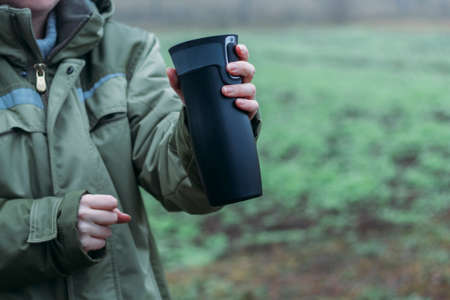 Women's hands are warming themselves on a black toggle switch with a hot drink in late autumn....