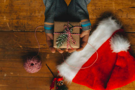 Christmas gift packaging. Hands wrap a small gift box in craft paper and a red-white string on the...