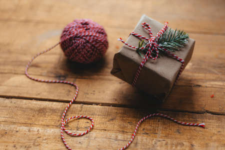 A Christmas gift box tied with a white and red ribbon, on a wooden rustic table, next to a packing rope. Packaging of Christmas gifts.の写真素材