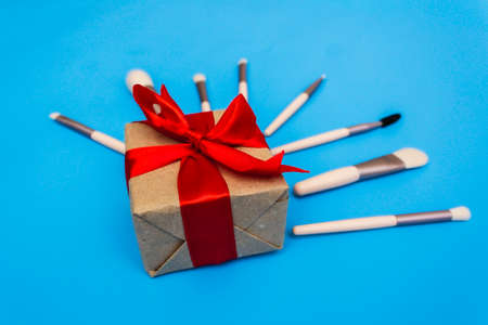 Gift box tied with a red ribbon on a blue background surrounded by makeup brushes.の写真素材
