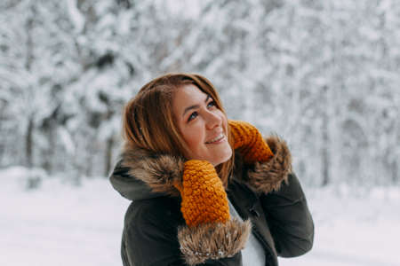 Portrait of a happy girl with a short haircut in mustard mittens in the forest after a snowfall. Christmas holidays, outdoor activities.の写真素材