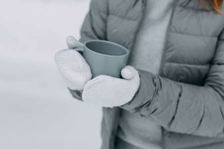 A man in the winter in the forest holds a gray mug with a hot drink in his hands. Warm and cozy in the winter park. selective focus.の写真素材