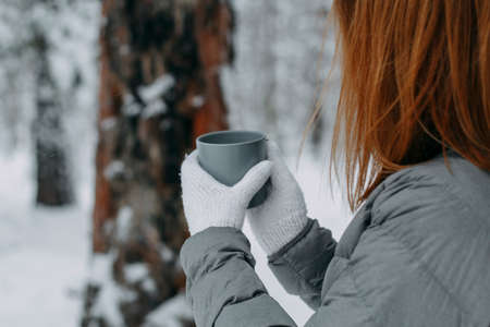 A man in the winter in the forest holds a gray mug with a hot drink in his hands. Warm and cozy in the winter park.selective focus.の写真素材